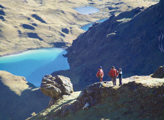 Rural shepherd boys, in their traditional red-woven ponchos, taking in the vista as they mind their grazing herd of alpaca & llama.